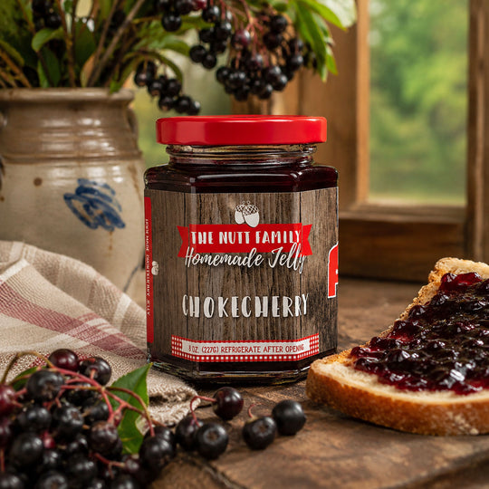 Jar of chokecherry jelly with a red lid on a wooden surface with toast and berries.