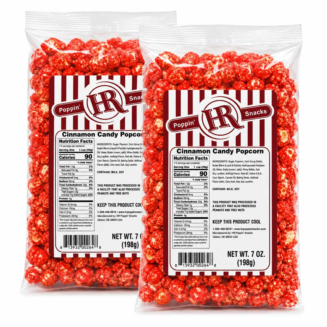 Two clear plastic bags of LR Snacks Cinnamon Candy Popcorn standing upright against a white background. The bags are filled with bright red candy-coated popcorn kernels and feature a white label with red and black stripes, the LR logo, and product details including nutrition facts and net weight 7 oz (199g).