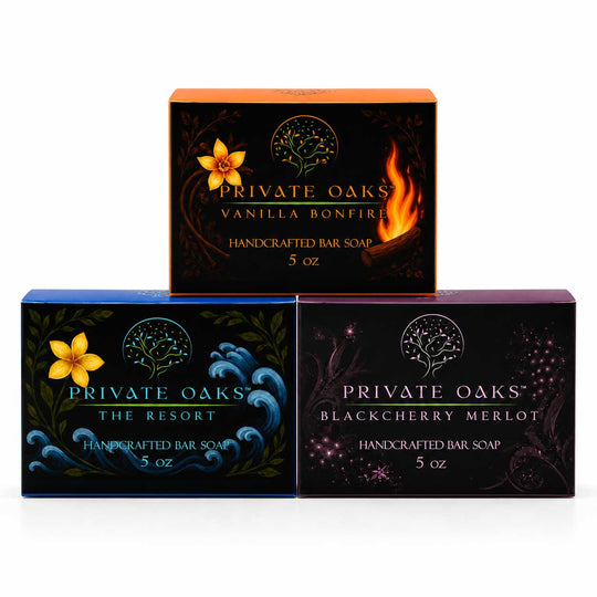 Three boxes of Private Oaks handcrafted bar soap arranged in a pyramid on a white background. The top box is Vanilla Bonfire with orange and black packaging, and the bottom boxes are The Resort Blackberry Merlot with blue and purple packaging.