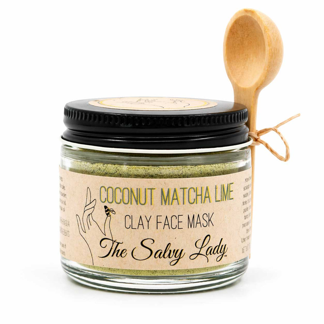 Jar of coconut matcha lime clay face mask with a wooden spoon on a white background