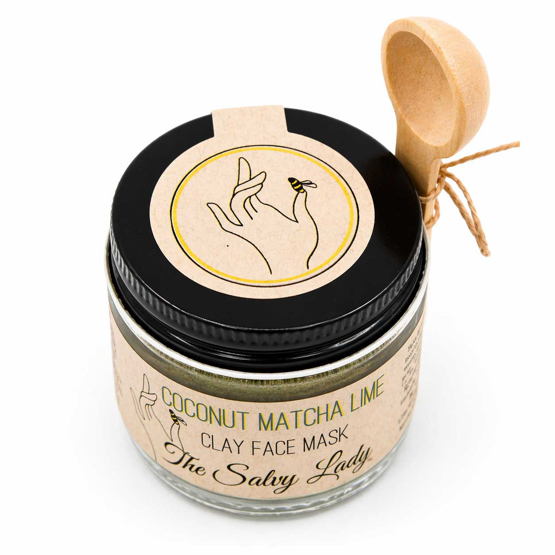 Jar of coconut matcha lime clay face mask with a wooden scoop on a white background