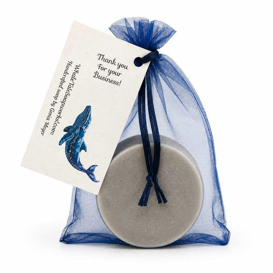 Round gray product in a blue drawstring bag with a card featuring a whale illustration on a white background