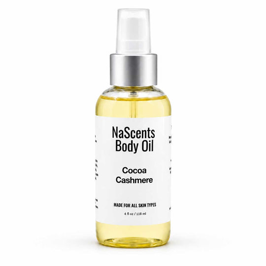 A bottle of NaScents Body Oil in the Cocoa Cashmere scent, featuring a clear bottle filled with pale yellow oil, a white label with black text, and a silver pump dispenser, set against a plain white background.