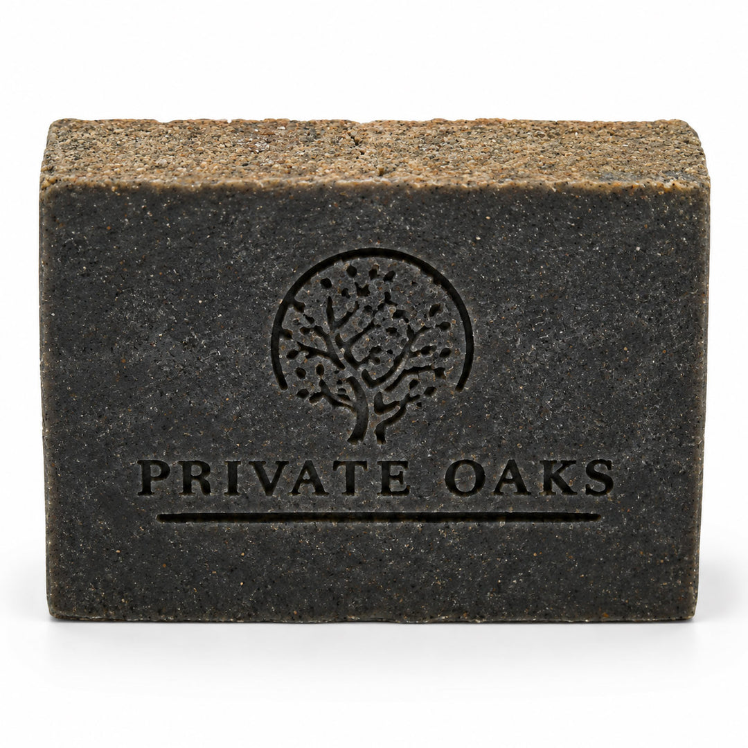 A rectangular dark charcoal gray soap bar with a textured, earthy brown top surface. The front is embossed with a tree logo and the brand name 'PRIVATE OAKS' in black, set against a clean white background.