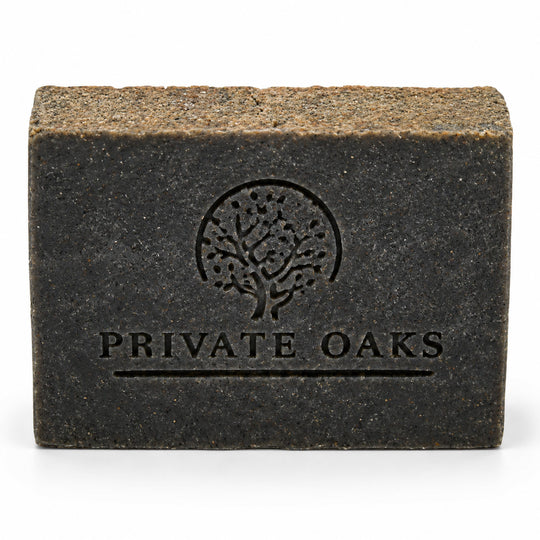 A rectangular dark charcoal gray soap bar with a textured, earthy brown top surface. The front is embossed with a tree logo and the brand name 'PRIVATE OAKS' in black, set against a clean white background.