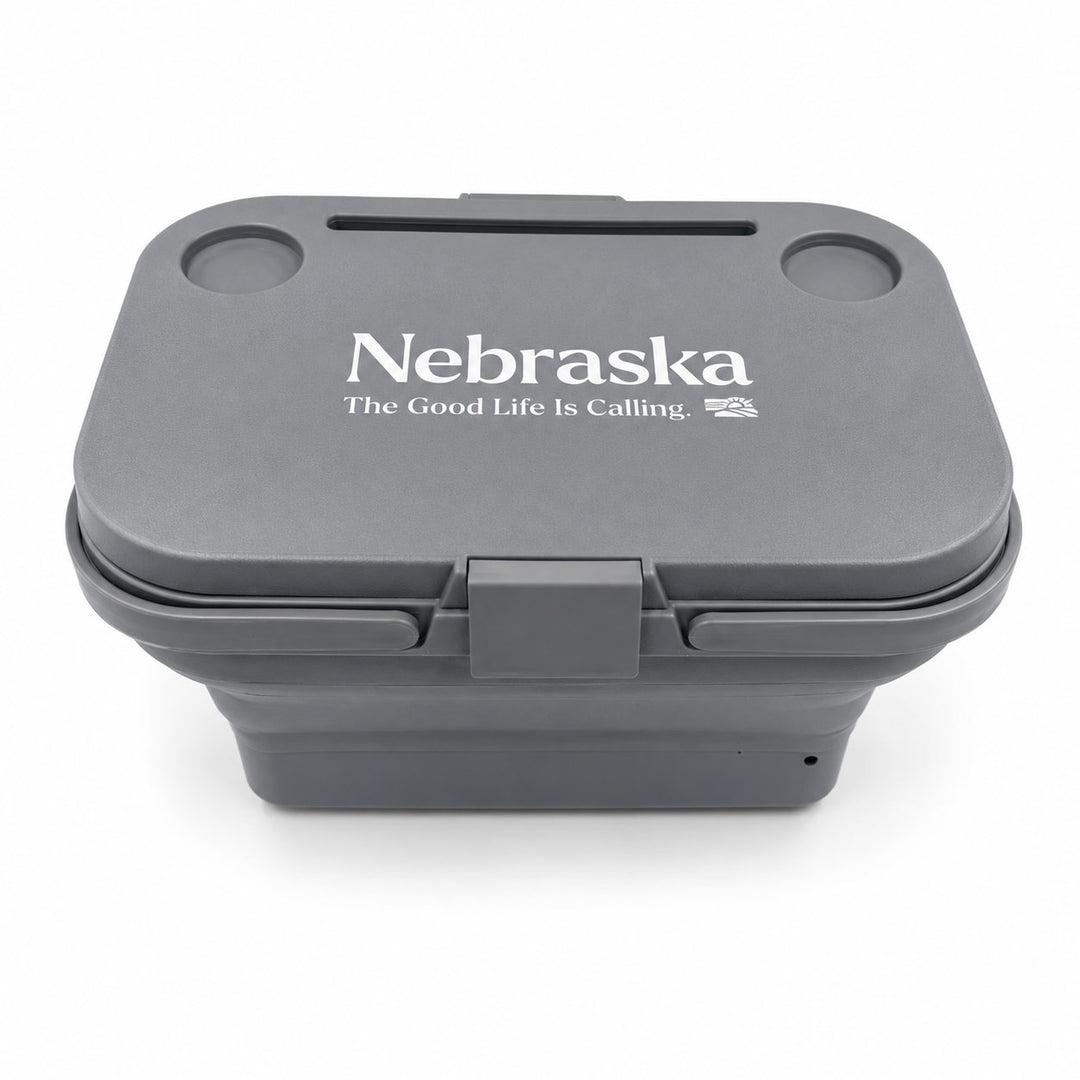 A dark gray collapsible container with a lid featuring the white printed text 'Nebraska' and 'The Good Life Is Calling.' on a clean white background.