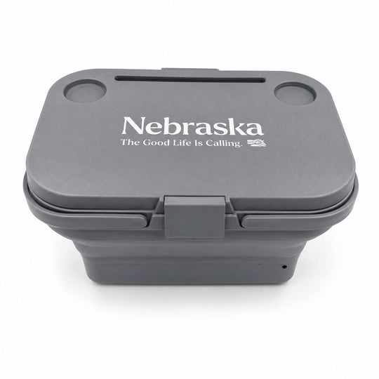 A dark gray collapsible container with a lid featuring the white printed text 'Nebraska' and 'The Good Life Is Calling.' on a clean white background.