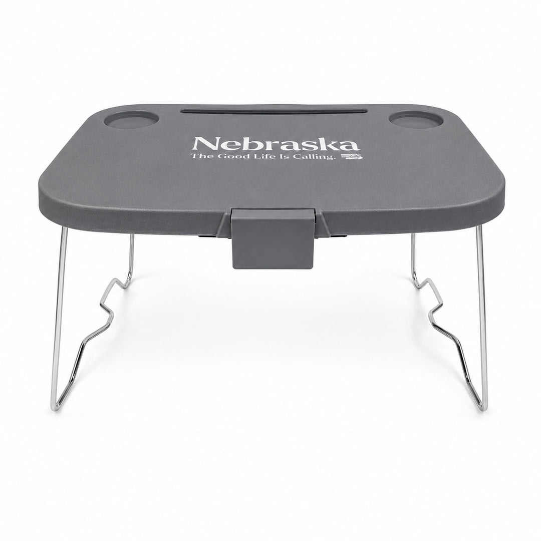 A dark gray portable lap desk with silver metal legs, featuring the white printed text 'Nebraska The Good Life Is Calling' on the top surface.