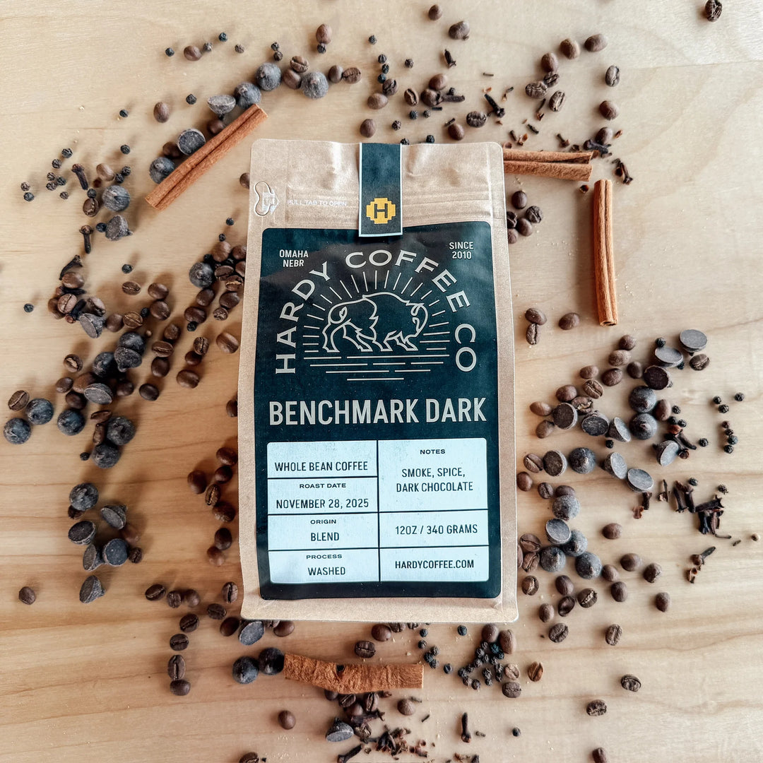 Hardy Coffee Co. Benchmark Dark coffee package on a wooden surface with coffee beans and cinnamon sticks.