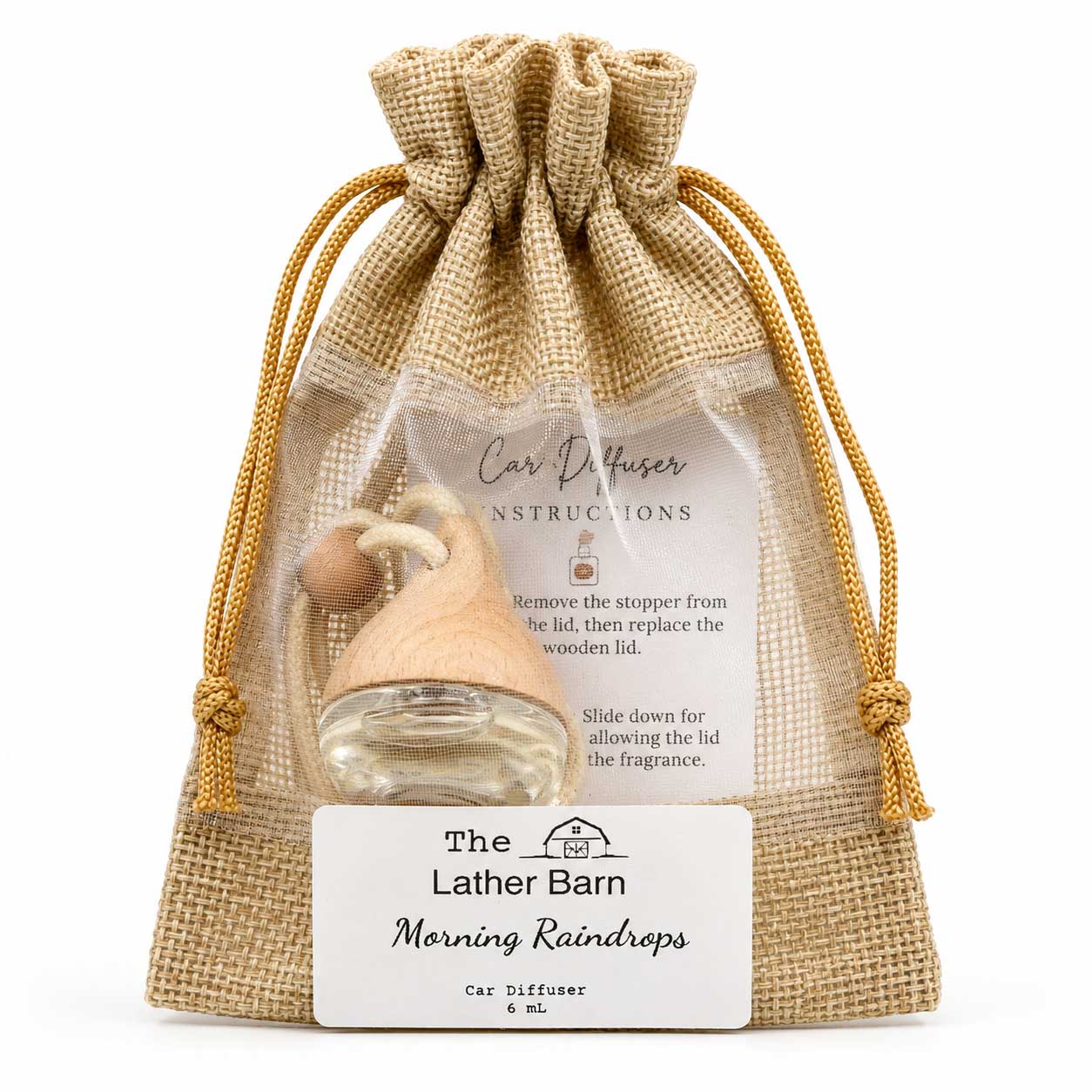A clear mesh drawstring pouch with a burlap-style front, holding a small clear glass car diffuser bottle with a light wood cap and wooden bead. A white label at the bottom reads 'The Lather Barn Morning Raindrops Car Diffuser 6 ml.
