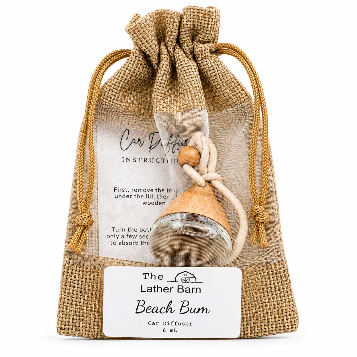 A small car diffuser bottle with a wooden bead and white cord, packaged inside a clear drawstring burlap pouch with a printed instruction card and a front label reading 'The Lather Barn Beach Bum Car Diffuser 6 ml'.
