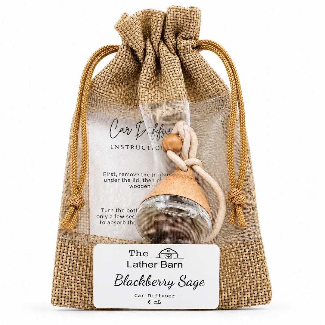 A small car diffuser in a clear glass bottle with a blackberry sage scent, packaged inside a natural burlap drawstring pouch. The pouch features a white label with instructions and the brand name 'The Lather Barn'.
