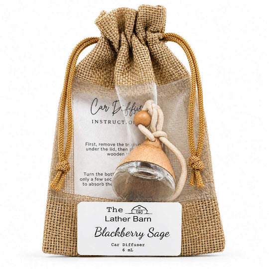 A small car diffuser in a clear glass bottle with a blackberry sage scent, packaged inside a natural burlap drawstring pouch. The pouch features a white label with instructions and the brand name 'The Lather Barn'.