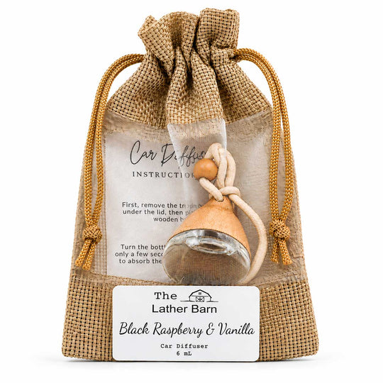 A car diffuser gift set in a burlap drawstring pouch with a wooden bell diffuser, a glass bottle, and an instruction card. The front label reads 'The Lather Barn Black Raspberry & Vanilla Car Diffuser 6 ml'.