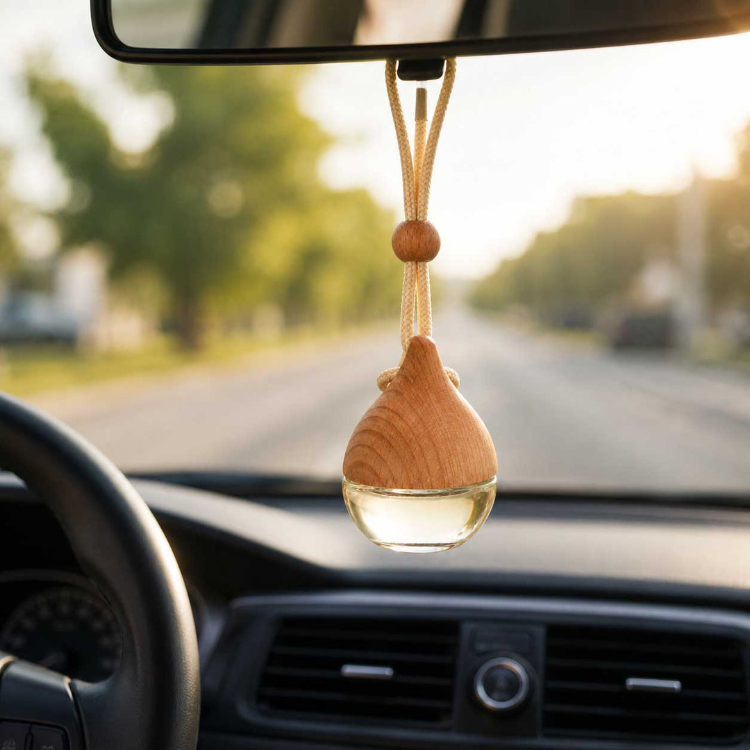 A wooden car air freshener hanging from a rearview mirror inside a car, with a blurred road and trees visible through the windshield.