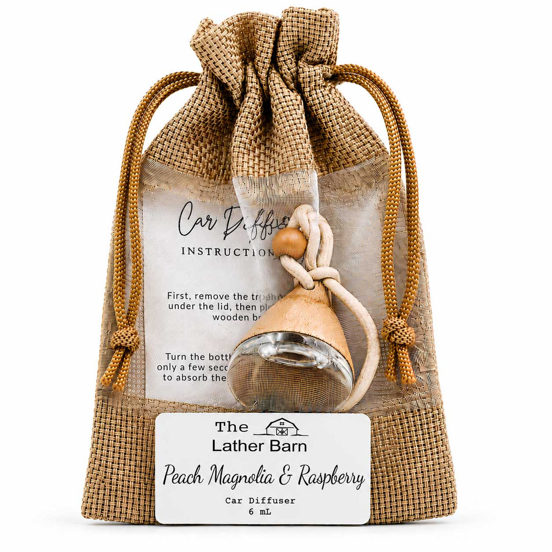 A car diffuser bottle with a wooden stopper and cord, packaged inside a clear drawstring burlap pouch with printed instructions and a front label reading 'The Lather Barn Peach Magnolia & Raspberry Car Diffuser & mL'.