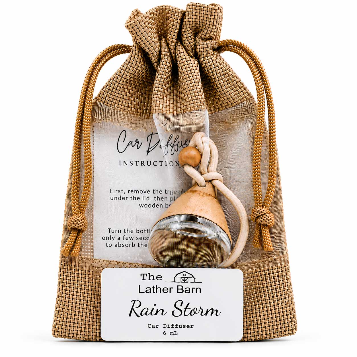 A small car diffuser bottle with a wooden top and metal diffuser head, packaged inside a tan burlap drawstring pouch. A printed instruction card is visible behind the product, and a white label at the bottom reads 'The Lather Barn Rain Storm Car Diffuser 6 mL'.