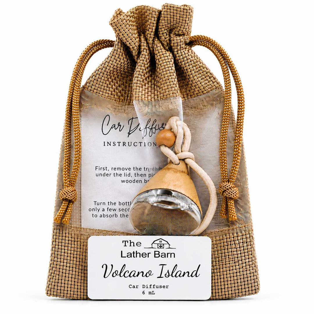 A car diffuser gift set from The Lather Barn Volcano Island, featuring a small glass car diffuser bottle with a wooden top, a beige rope, and a burlap drawstring pouch with an instruction card and a white brand label.