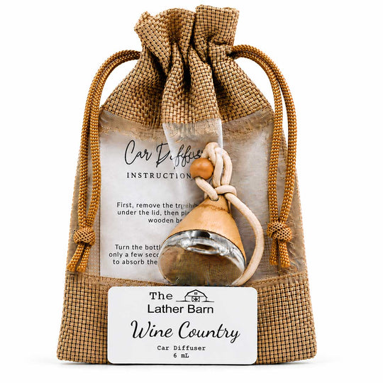 A car diffuser gift set from The Lather Barn, featuring a small wooden car diffuser bottle with a metal diffuser head, tied to a burlap drawstring pouch with an instruction card and a 'Wine Country' flavor label.