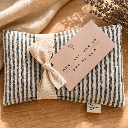 Striped eye pillow with a tag from The Lavender Co. on a wooden surface