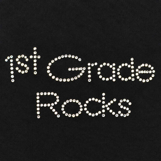 White rhinestone lettering that reads '1st Grade Rocks' on a black fabric background.