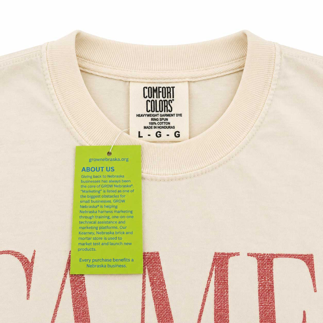 Close-up of a cream-colored Comfort Colors t-shirt with a green brand hangtag, showing the inner neck label and part of the red graphic print.