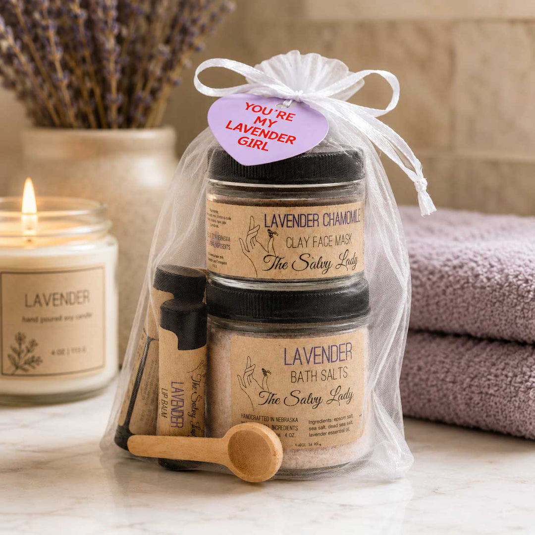 Set of lavender-themed skincare products with a candle and towel in the background
