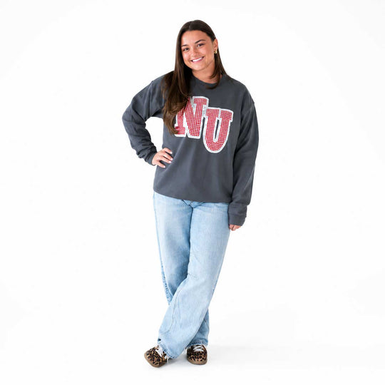 A woman modeling a dark gray crewneck sweatshirt with a red and white 'NU' graphic on the front, paired with light blue jeans and leopard print shoes, against a plain white background.