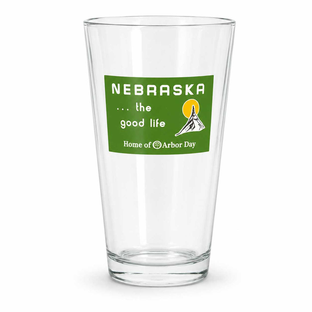 A clear glass pint glass with a green printed label that reads 'NEBRASKA .