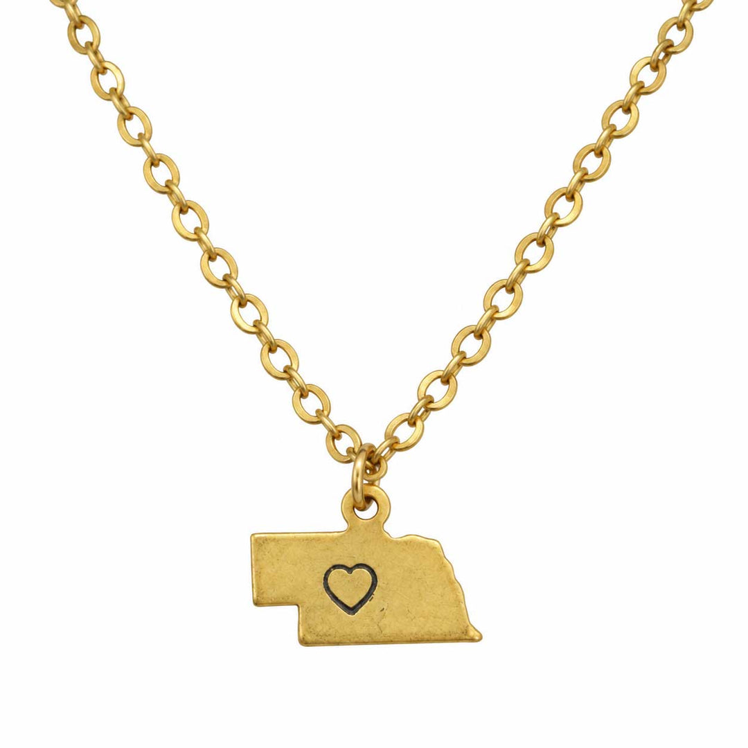 A gold chain necklace with a pendant shaped like the state of Nebraska, featuring a small heart outline engraved in the center, shown against a plain white background.