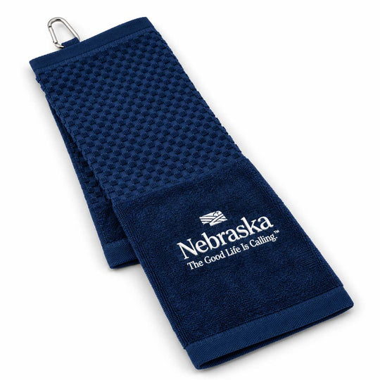 A navy blue waffle-weave golf towel with a silver metal clip at the top and white embroidered Nebraska text and logo on a white background.