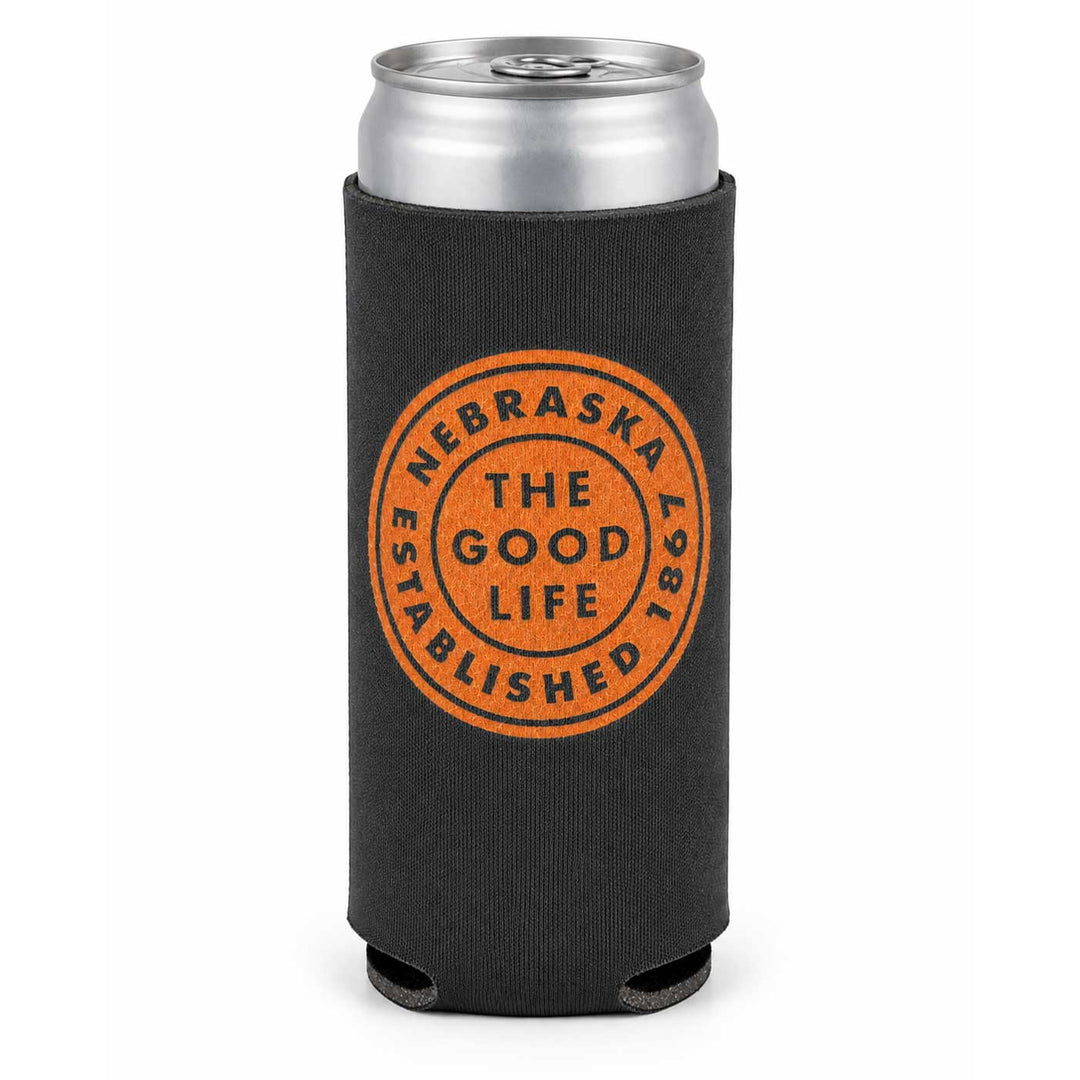 A black neoprene can cooler sleeve with a silver aluminum can inserted, featuring an orange circular stamp design that reads 'NEBRASKA 2025 THE GOOD LIFE ESTABLISHED'.