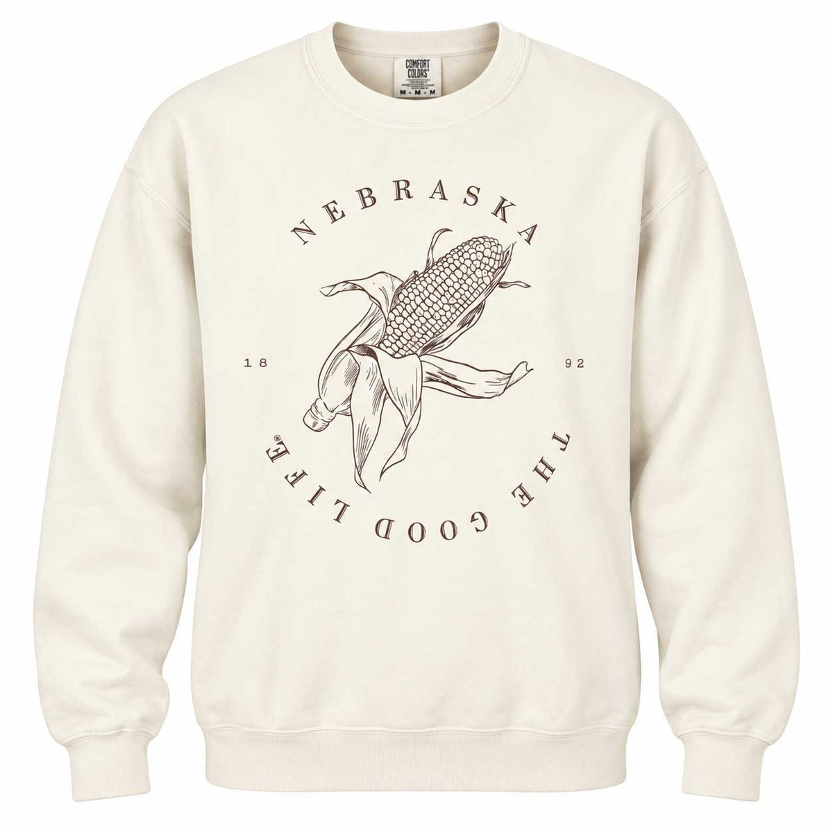 An off-white crewneck sweatshirt featuring a dark brown graphic of a corn cob with a person dancing in front of it, surrounded by the text 'NEBRASKA THE GOOD LIFE 1992'.
