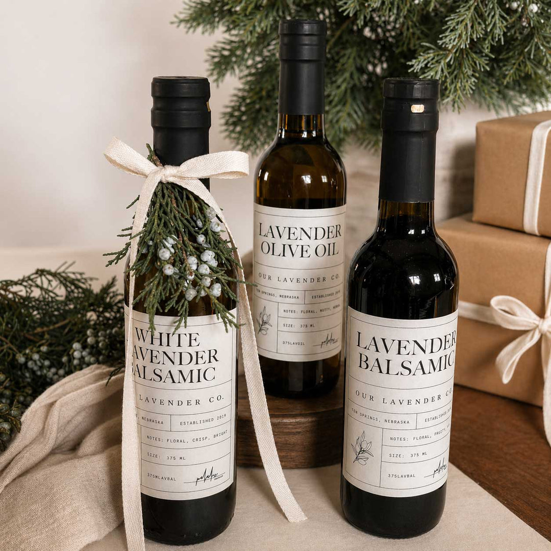 Three bottles of lavender-infused olive oil and balsamic vinegar on a table with a festive background.