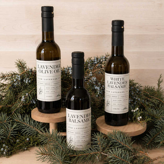 Three bottles of lavender-infused olive oil and balsamic on wooden stands with a Christmas tree background.