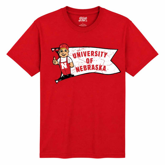 A red short-sleeve crewneck t-shirt featuring a University of Nebraska graphic on the chest, including the mascot Nebraskan and a banner reading 'UNIVERSITY OF NEBRASKA'.