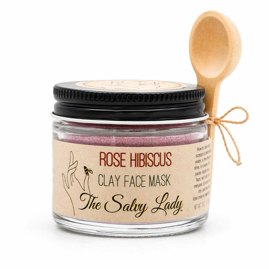 Jar of Rose Hibiscus Clay Face Mask from The Salvy Lady with a wooden spoon on a white background