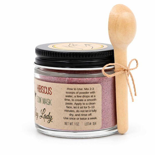 Jar of hibiscus clay mask with a wooden spoon on a white background