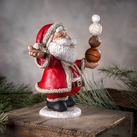 Santa Claus figurine holding basketballs on a wooden platform with a Christmas tree in the background