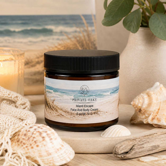 A jar of Private Oaks Island Escape Face And Body Cream sits on a wooden board surrounded by seashells, driftwood, a candle, and a beach scene backdrop.