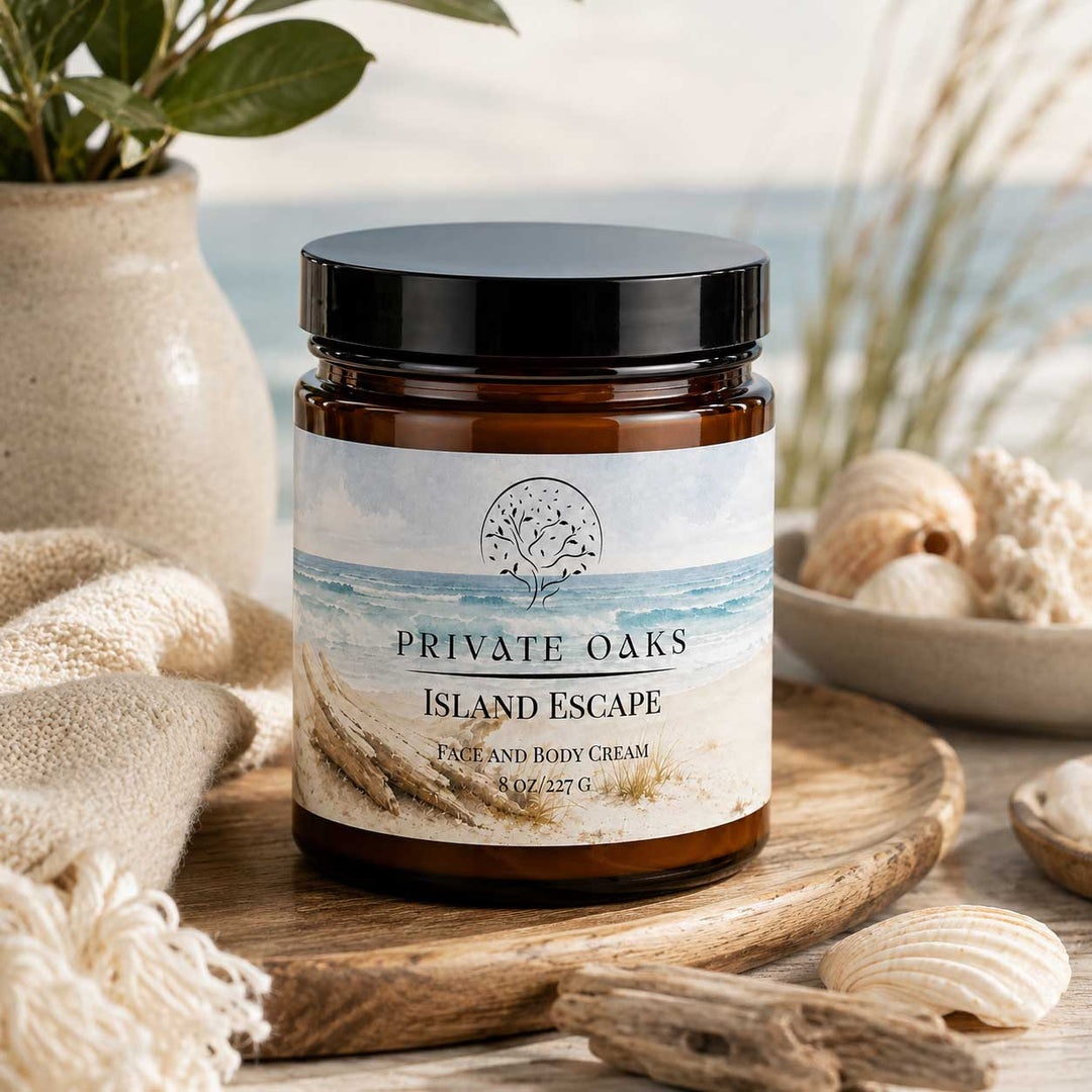 An amber glass jar of Private Oaks Island Escape Face and Body Cream sits on a wooden tray surrounded by seashells, a textured towel, and a blurred beach background.