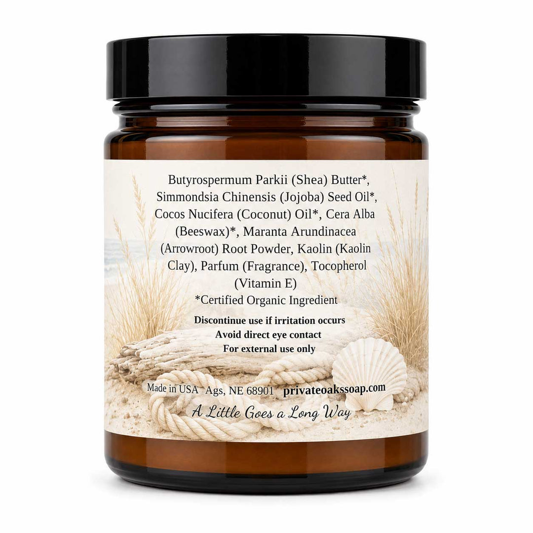 An amber glass jar of Private Oak Soap Butyrospermum Parkii (Shea) Butter, featuring a black screw cap and a cream-colored label with beach-themed illustrations of seashells and sand. The label lists various organic ingredients and product details.