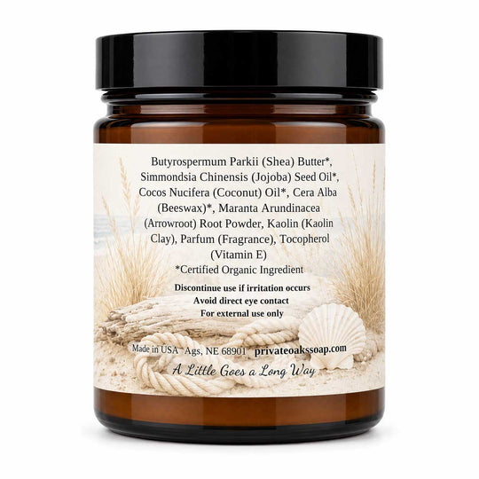 An amber glass jar of Private Oak Soap Butyrospermum Parkii (Shea) Butter, featuring a black screw cap and a cream-colored label with beach-themed illustrations of seashells and sand. The label lists various organic ingredients and product details.