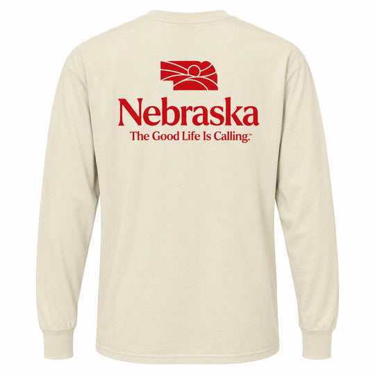 A cream-colored long-sleeve t-shirt shown from the back, featuring a red graphic of the state of Nebraska with a rising sun and the text 'Nebraska The Good Life Is Calling:' printed in red.