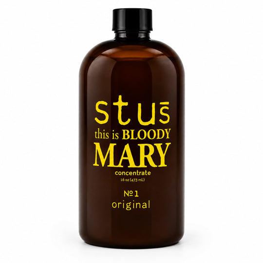 An amber brown bottle with a black cap, featuring yellow text that reads 'stus this is BLOODY MARY concentrate' on a clean white background.