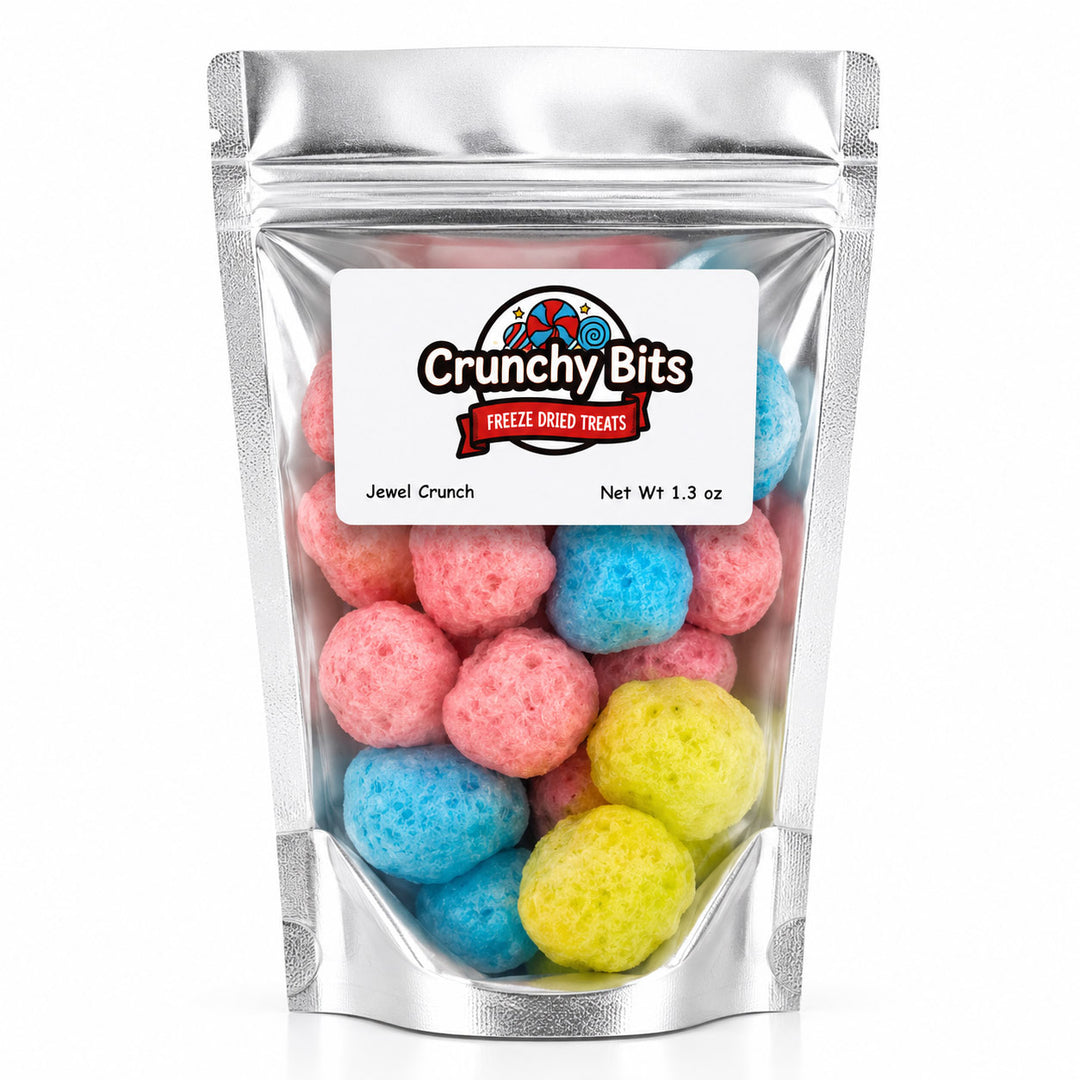 A silver stand-up pouch of Crunchy Bits Freeze Dried Treats, specifically Jewel Crunch, filled with colorful freeze-dried gummy candies in pink, blue, and yellow, set against a plain white background.