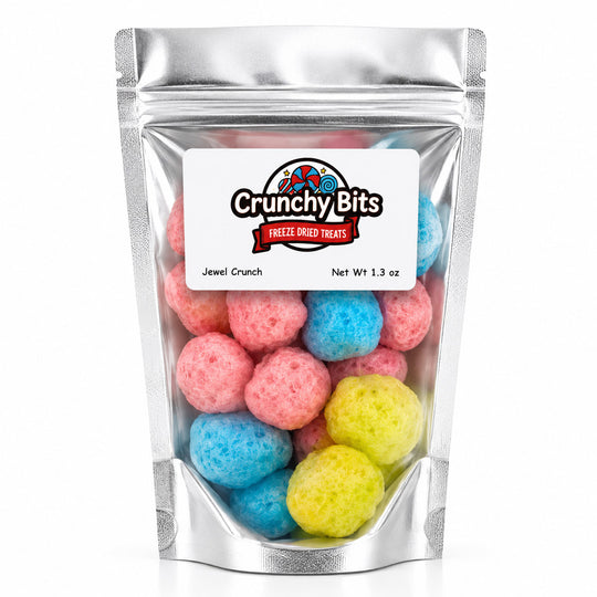 A silver stand-up pouch of Crunchy Bits Freeze Dried Treats, specifically Jewel Crunch, filled with colorful freeze-dried gummy candies in pink, blue, and yellow, set against a plain white background.