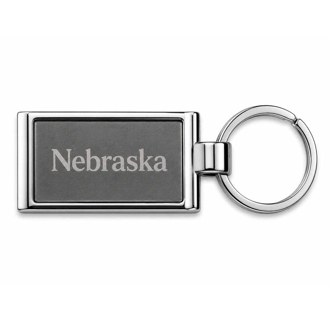 A rectangular metal keychain with a dark gray engraved face reading 'Nebraska' and a shiny silver-toned split ring, shown on a plain white background.