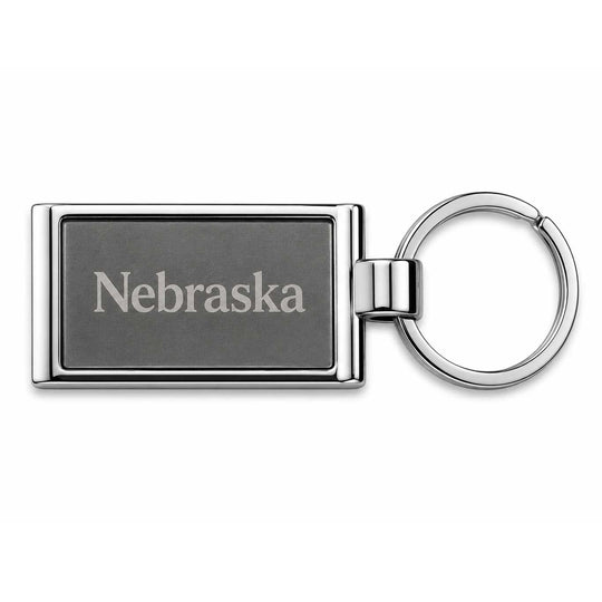 A rectangular metal keychain with a dark gray engraved face reading 'Nebraska' and a shiny silver-toned split ring, shown on a plain white background.
