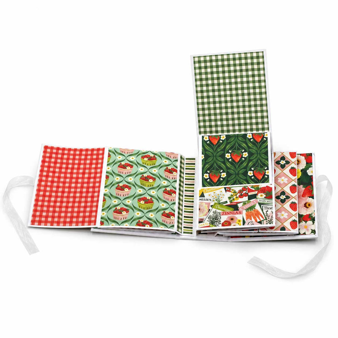 A fabric journal or scrapbook album with multiple patterned covers laid open on a white background. The visible covers include red and white gingham, green and white gingham, a green patterned cover with red hearts, striped bands, floral and fruit motifs, and a diamond-patterned cover.